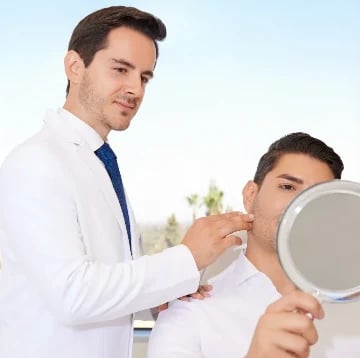 Surgeon in a white coat reviewing a patient's profile while the patient holds a hand mirror